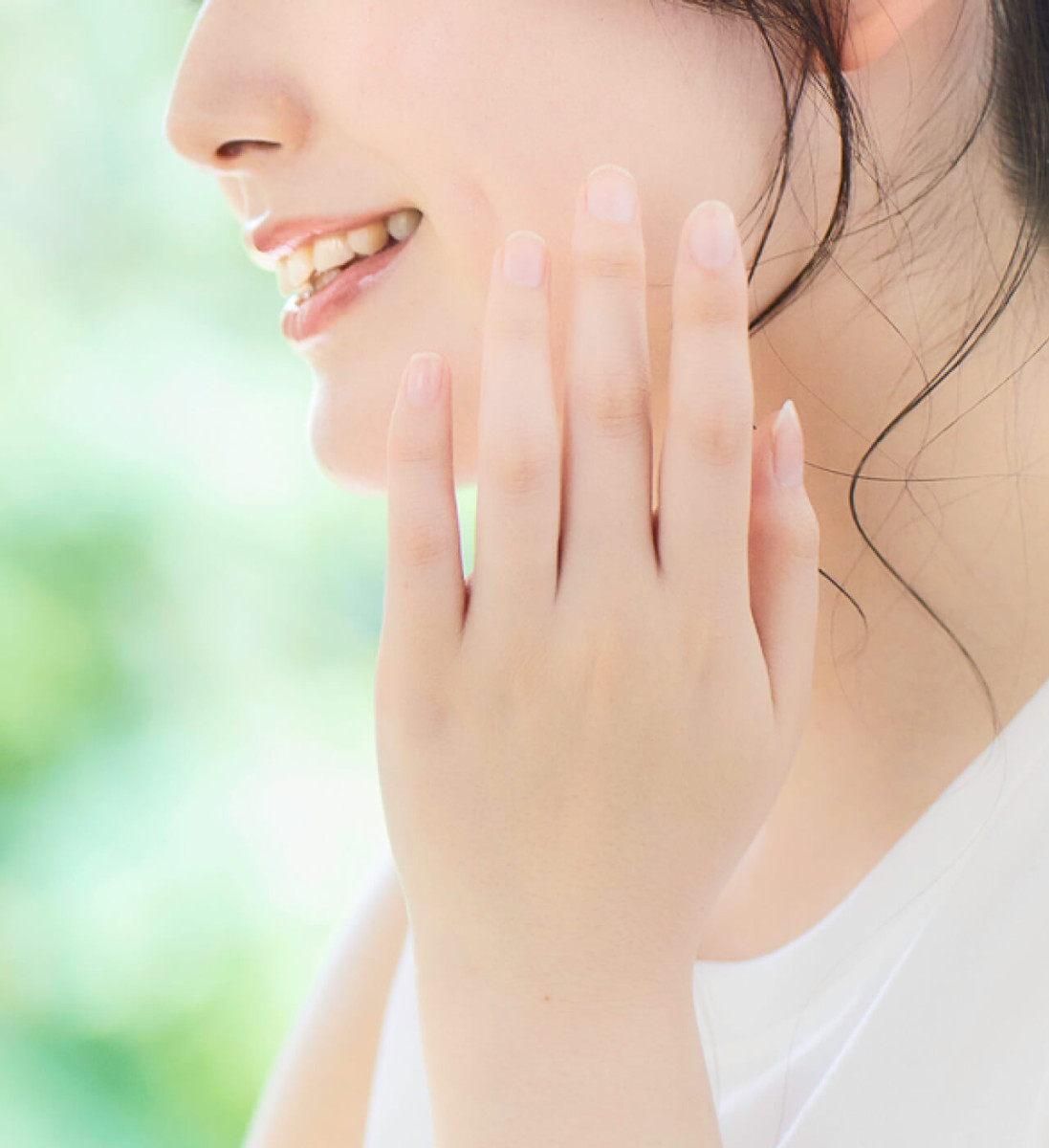 穏やかな笑顔で自身の頬に優しく指先を添える女性の口元。